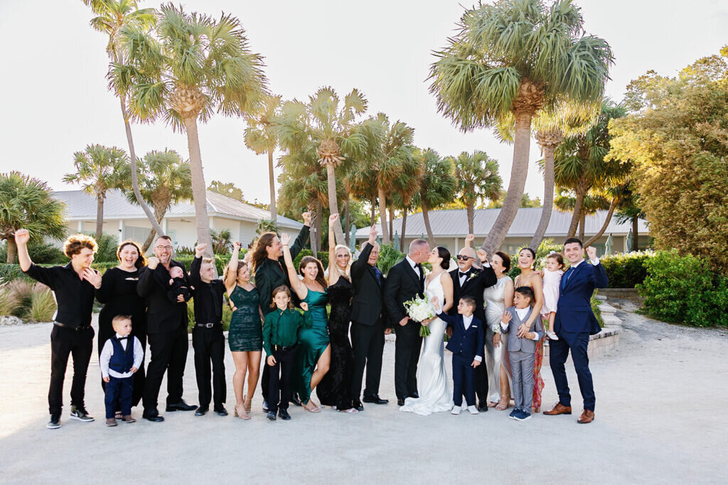 The bride and groom share a fun and lively moment with their wedding party, surrounded by lush palm trees and golden sunlight in the Florida Keys. Captured by Claudia Amalia Photography, a destination wedding photographer.