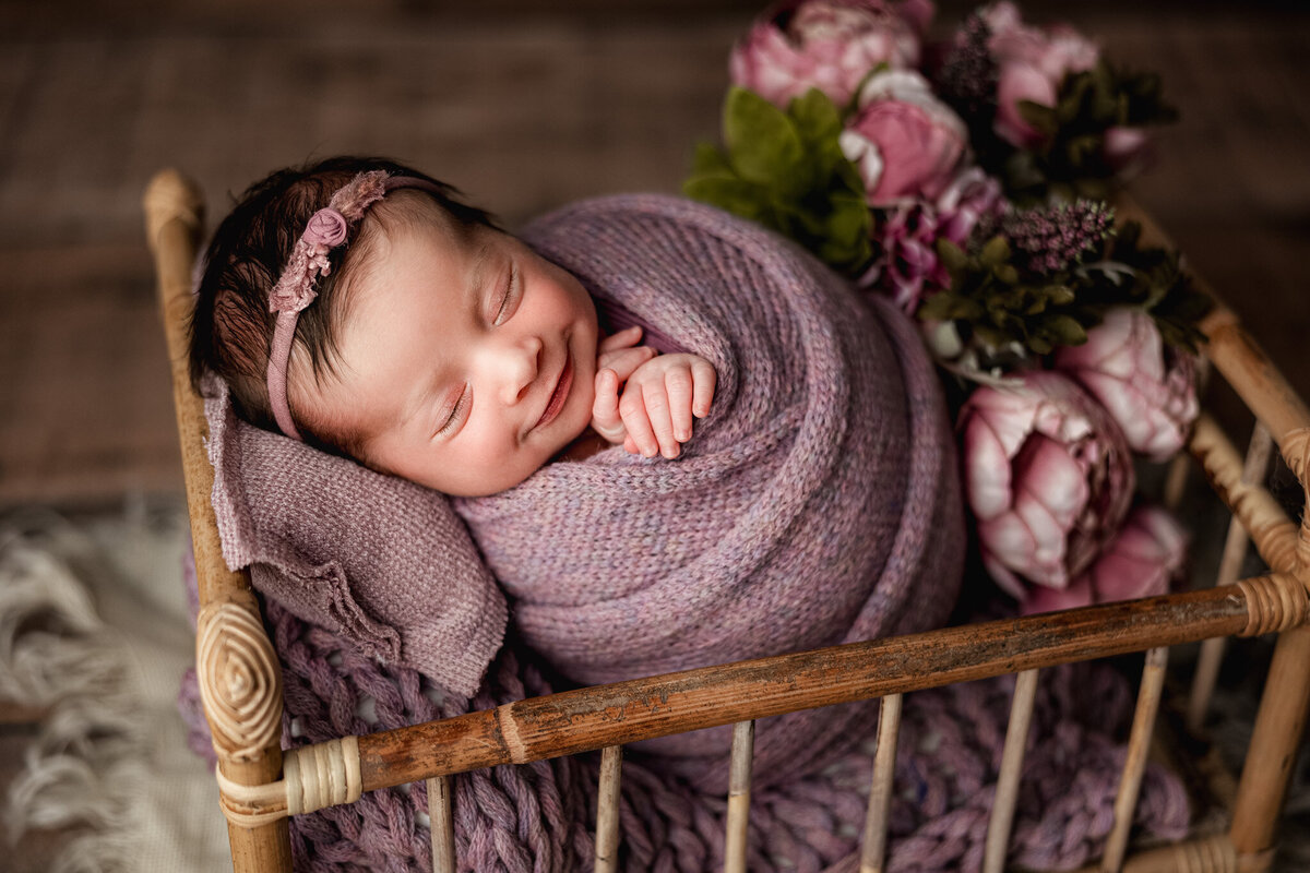 Newborn baby swaddled in hand knit blanket, smiling and sleeping peacefully in East Jordan studio