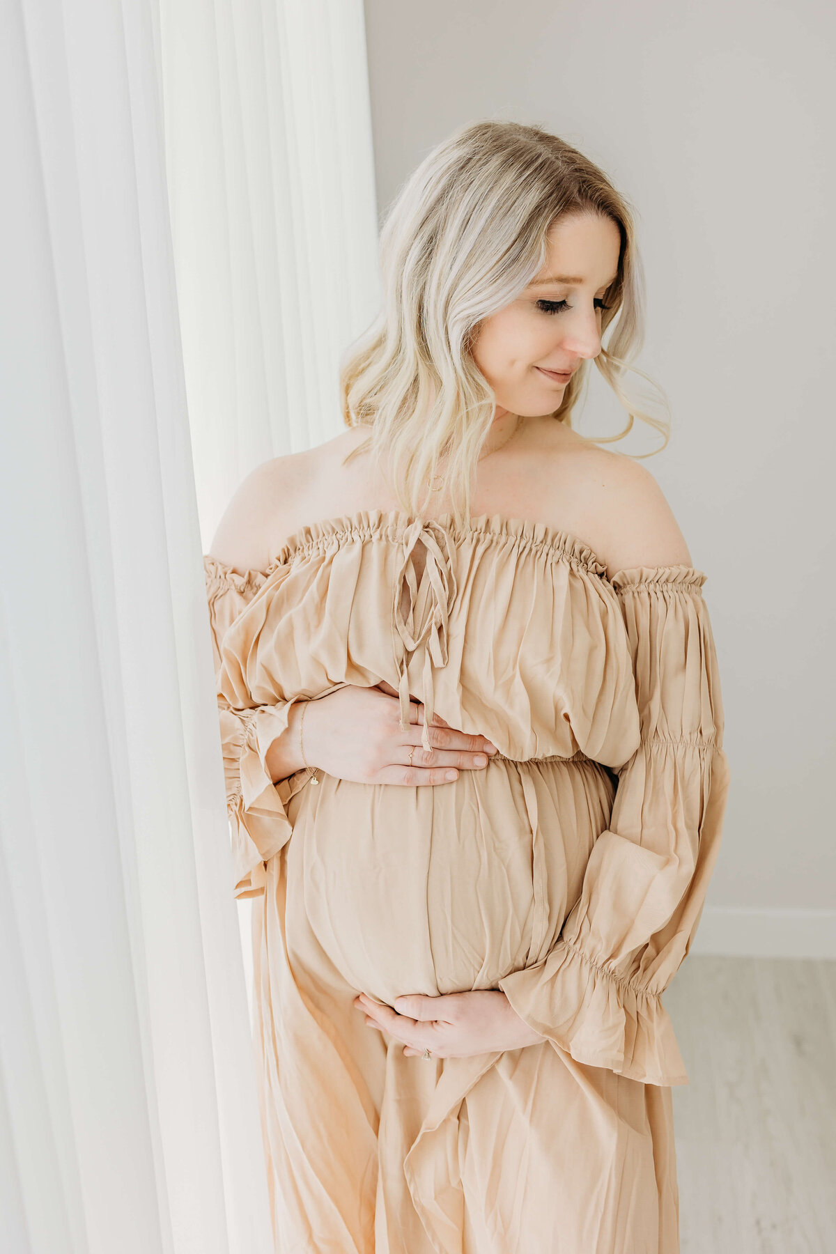 Blonde mom in beige dress holding belly expecting son