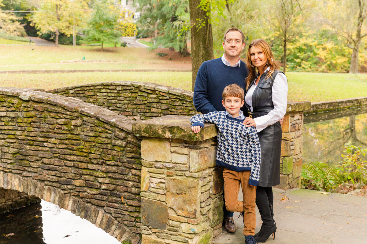 parents and son standing on a bridge in a park