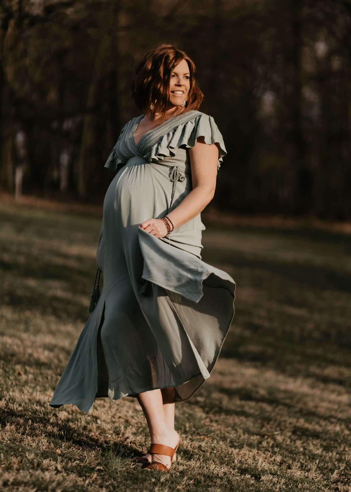 A pregnant woman in a sage green dress poses beautifully in a field for a Pittsburgh maternity photographer.