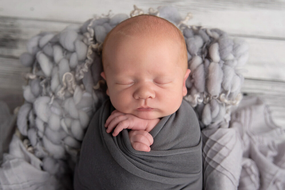 newborn baby boy wrapped in grey for his baby pictures.