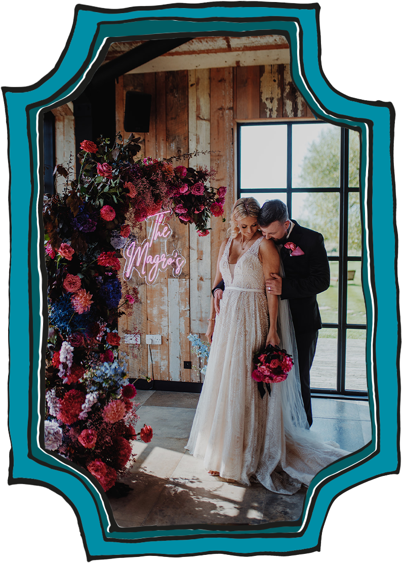 Wedding couple posing in front a neon sign with their surname and the wedding florals.