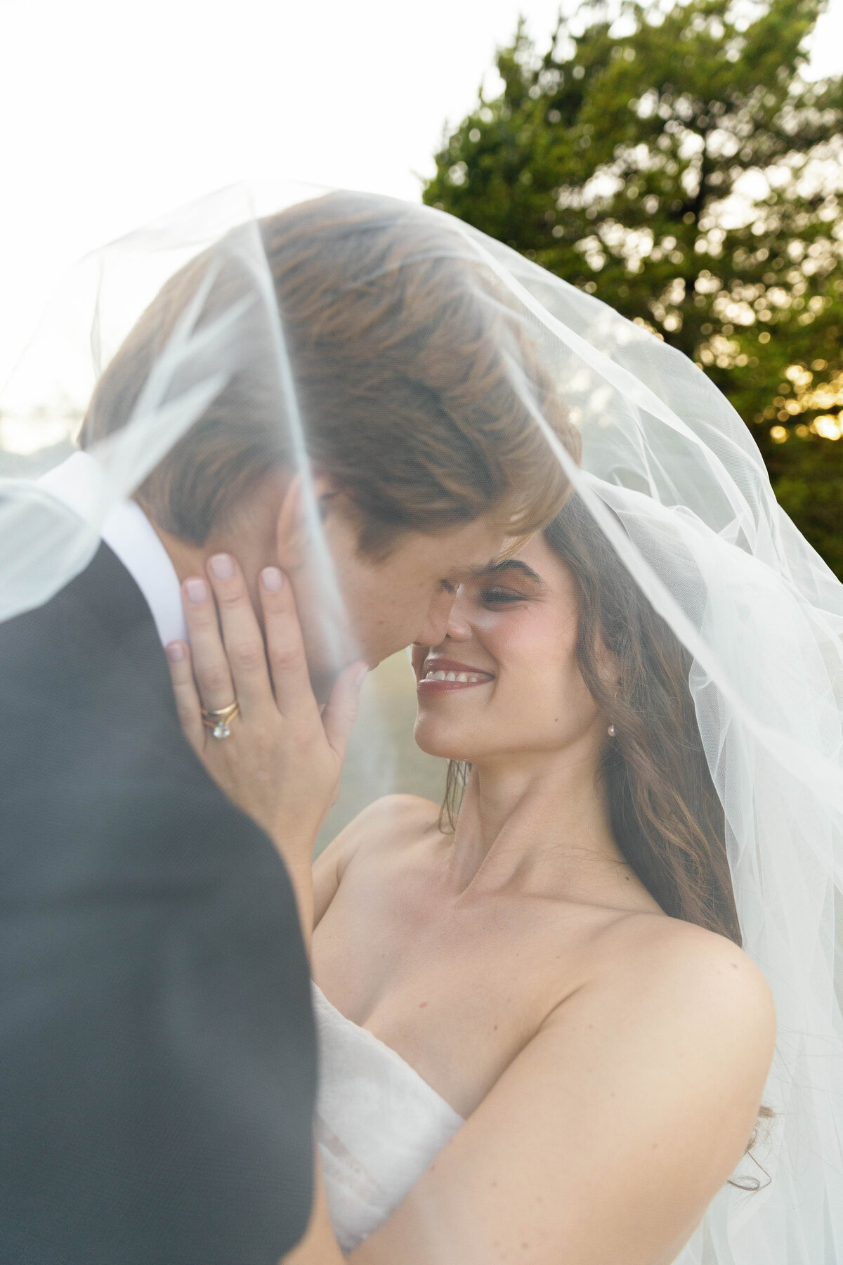 Tender close-up of bride and groom sharing an intimate moment under the wedding veil at golden hour, featuring the bride’s soft pastel bouquet created by an Arkansas wedding florist.