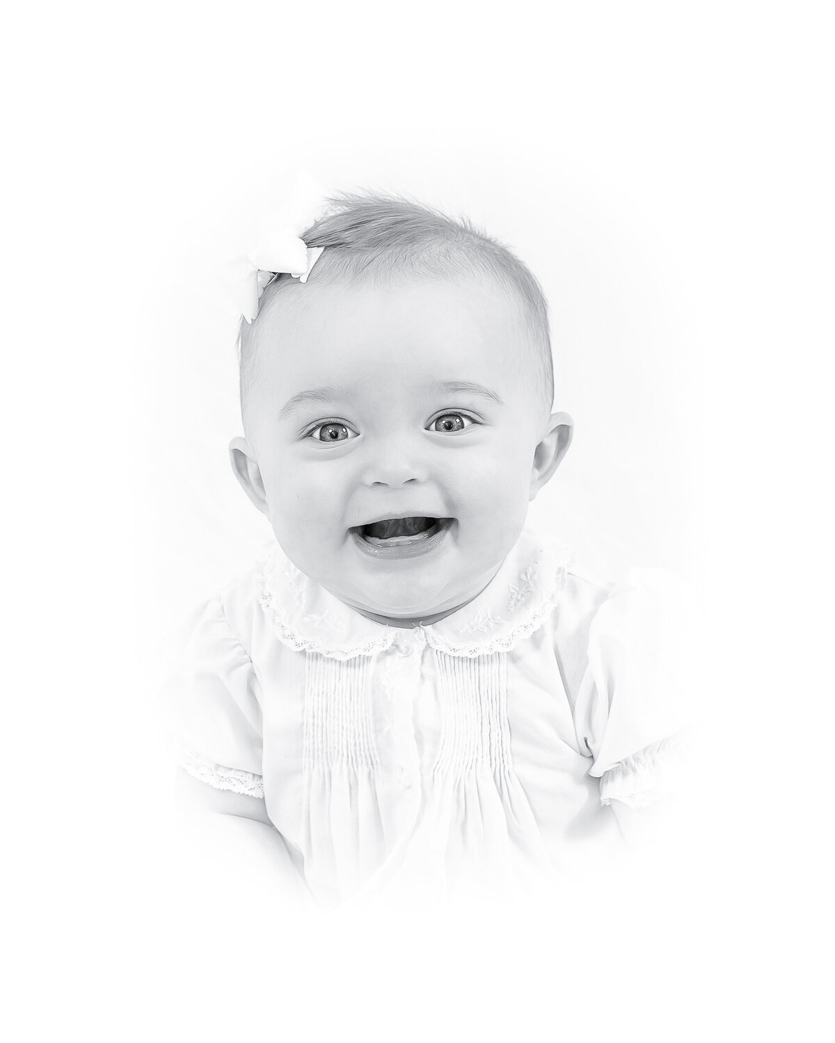 Black and white heirloom portrait of a smiling baby dressed in a classic white outfit with lace details. This timeless baby photography captures the innocence and joy of childhood, created by a Birmingham newborn photographer specializing in elegant, light-filled portraits.