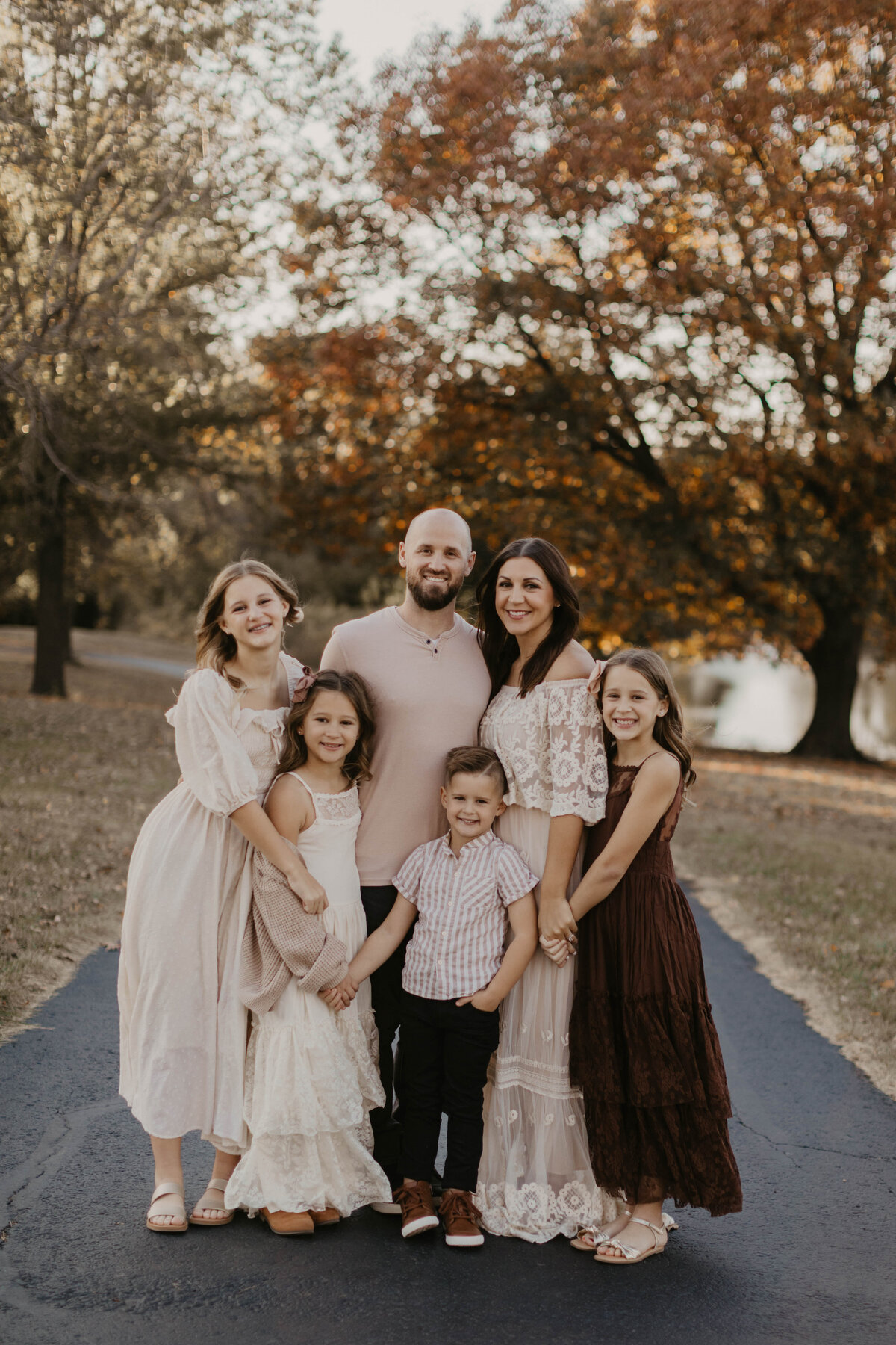 Parents with four children smiling at the camera in front of fall foliage.