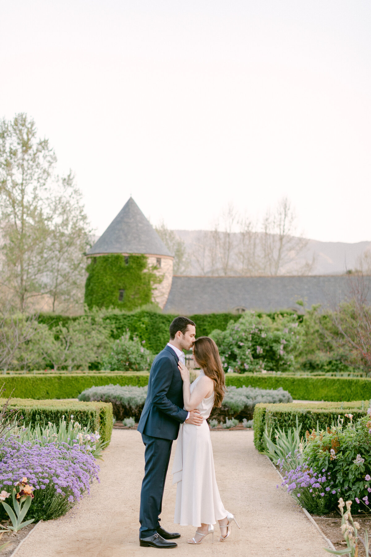 Groom-to-be kisses his bride's forehead in outdoor gardens
