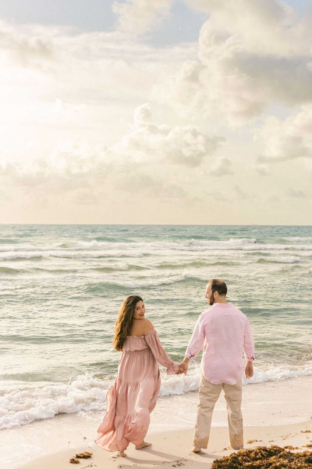 Expectant couple strolling along the shoreline in South Florida with the mom looking back.