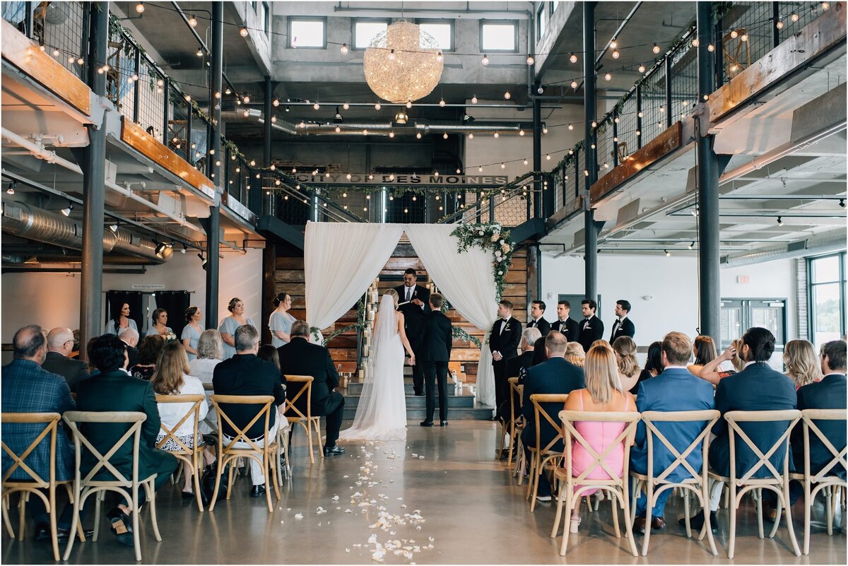 Bride and Groom stand at the aisle during their ceremony at The River Center in DSM, IA. Photos by Anna Brace, a Des Moines Iowa Wedding Photographer.