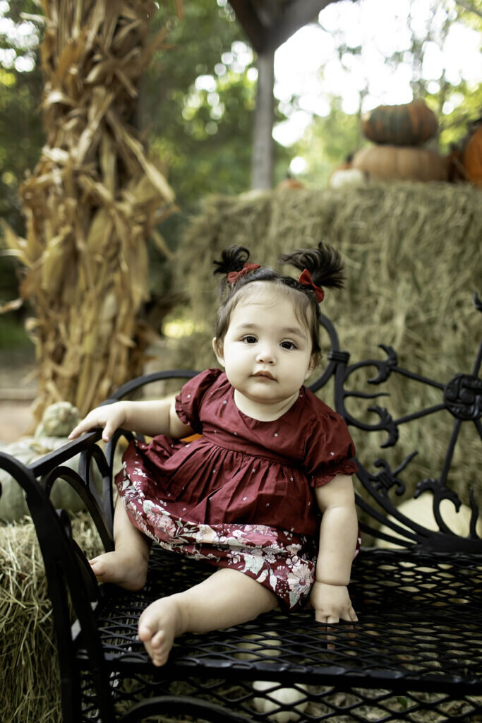 One-year-old girl wearing a simple dress, sitting on the floor and looking at the camera with a soft smile