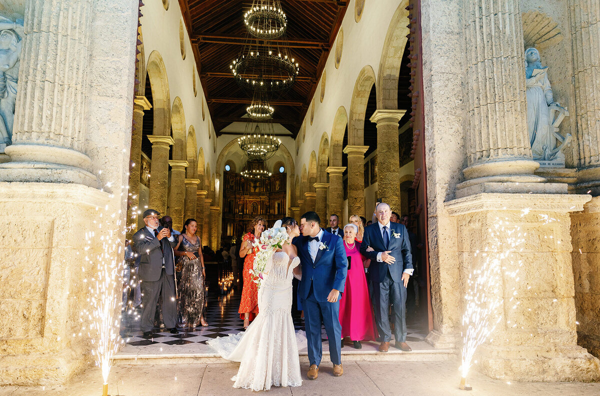 Victoria and Daniel joyfully exit the church after their Cartagena wedding ceremony, with candles lining the aisle and guests applauding.