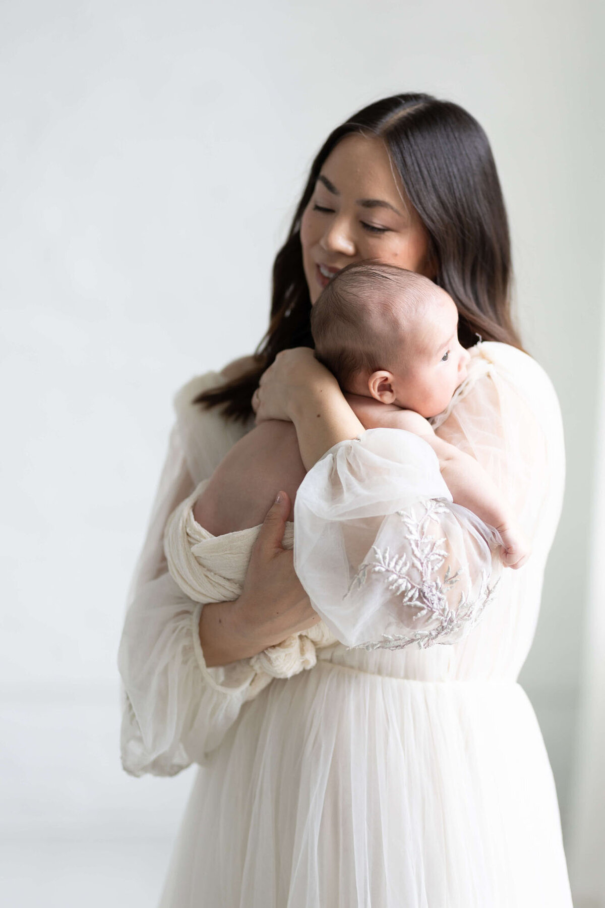 Mother cradling newborn in arms during intimate Bay Area newborn photography session.