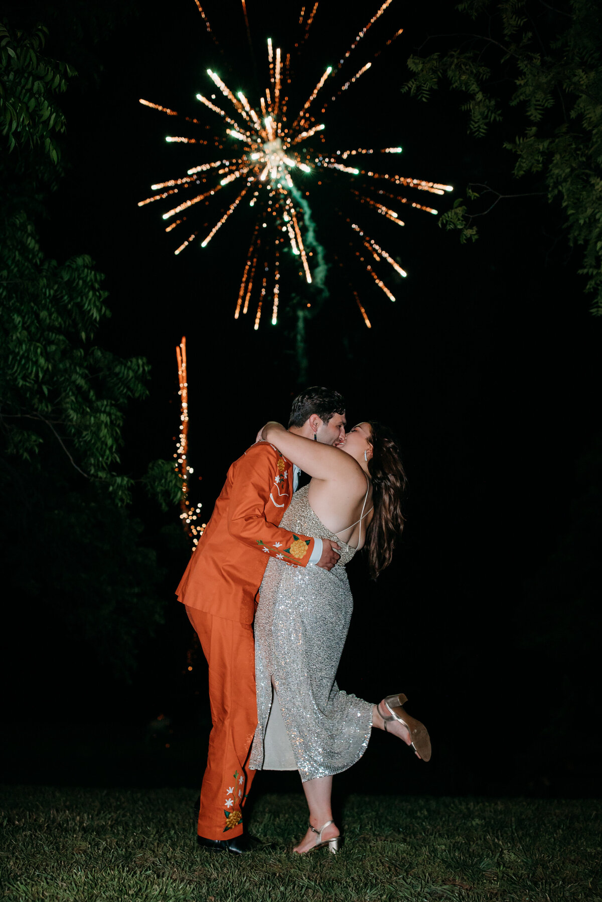 Couple kissing in a nighttime celebration with fireworks bursting in the sky above