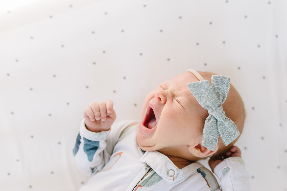 baby yawning in crib with green bow on head