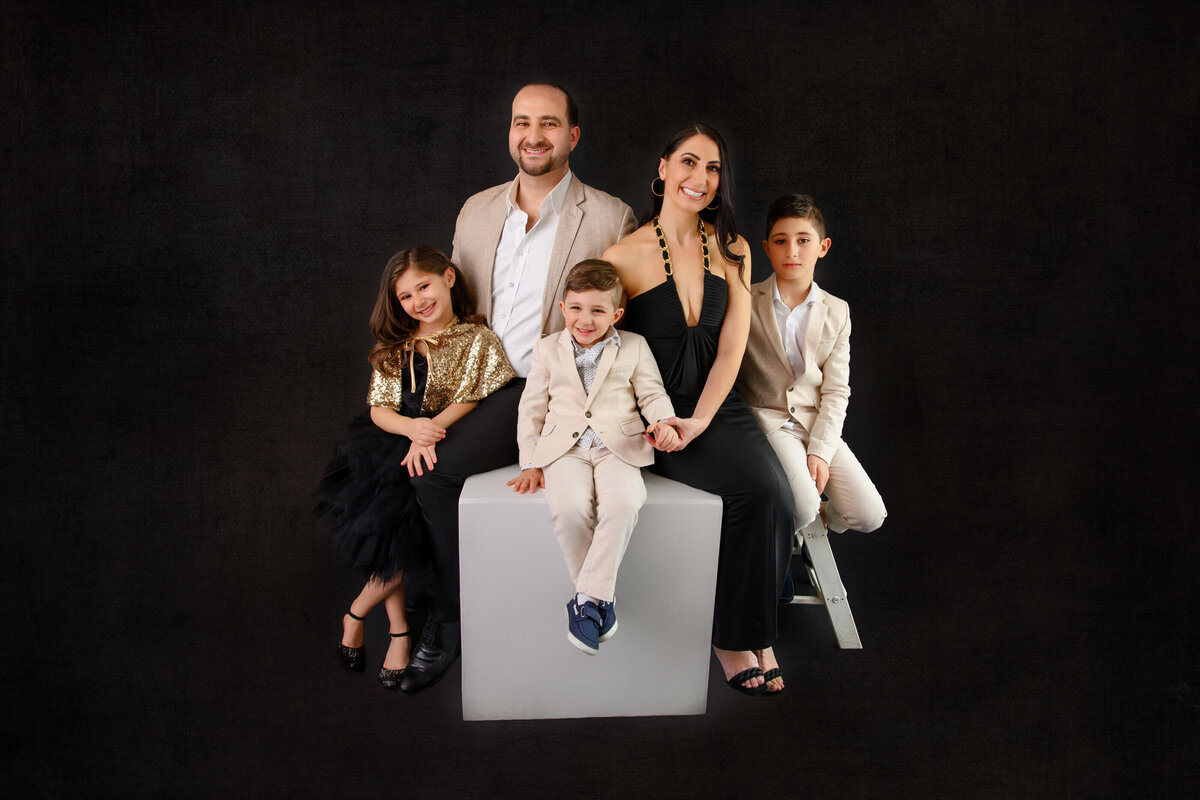 Family photo of a family of 5 consisting of mom and dad, two sons and a daughter on a black background
