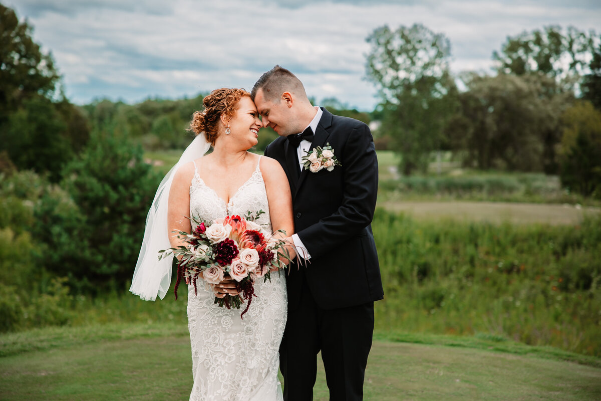Newlyweds touch foreheads while snuggling and standing in a lawn