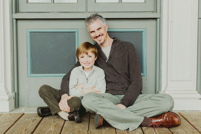 Dad sits on the ground with son next to him smiling at the camera