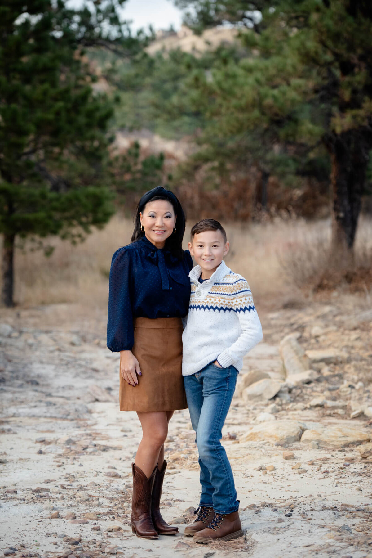 A mother in a blue top and brown skirt hugs her son in a white sweater for a Denver family photographer