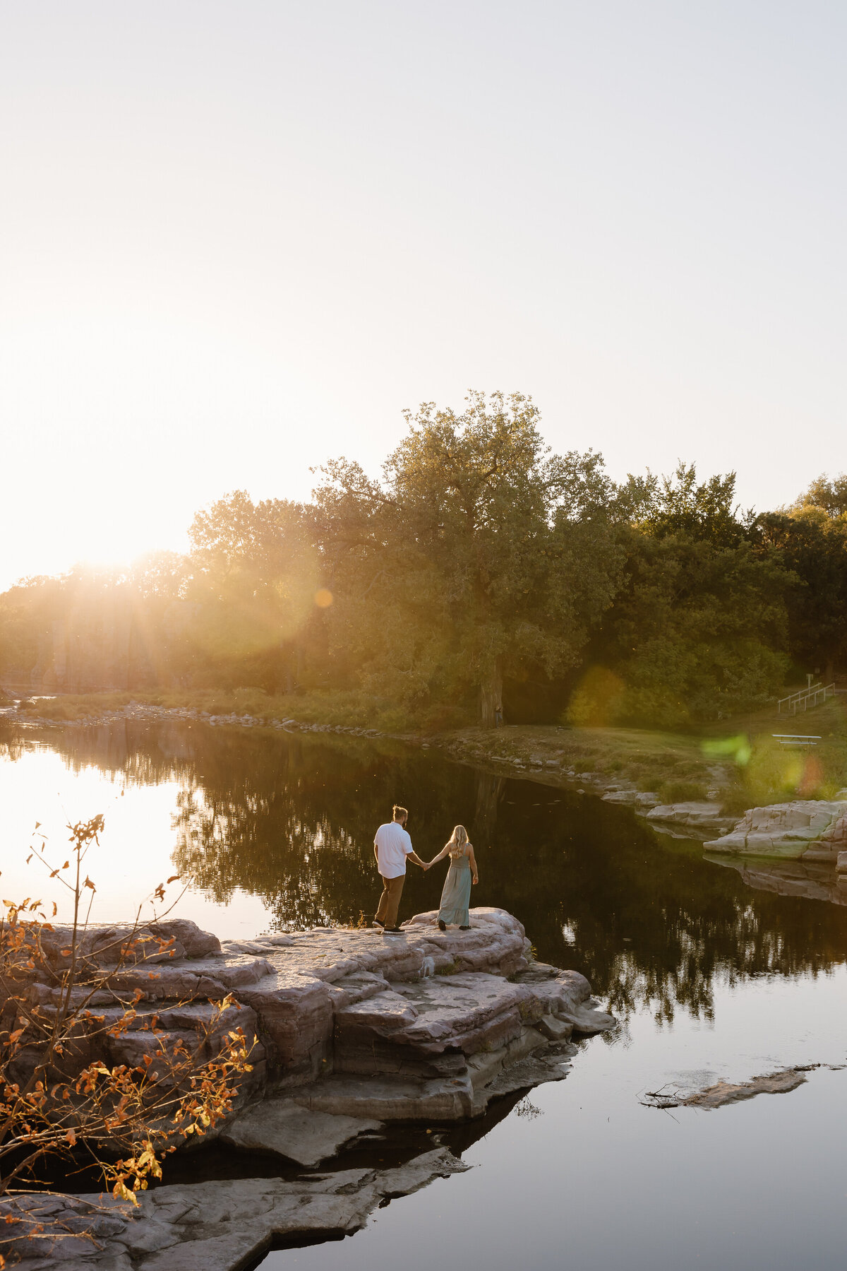 A couple standing on a rock overlooking a pond and holding hands