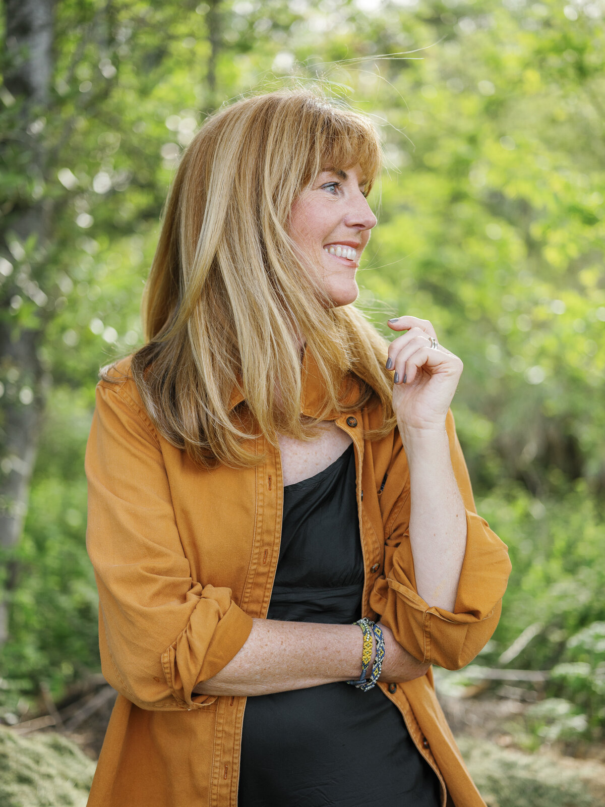 Natural outdoor portrait of a blonde woman in an orange jacket, looking to the side and smiling during a New York City brand photography session.