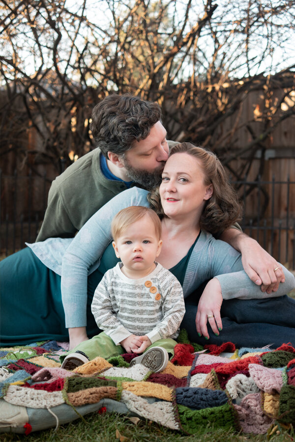 Family sitting on a quilted blanket in the fall.