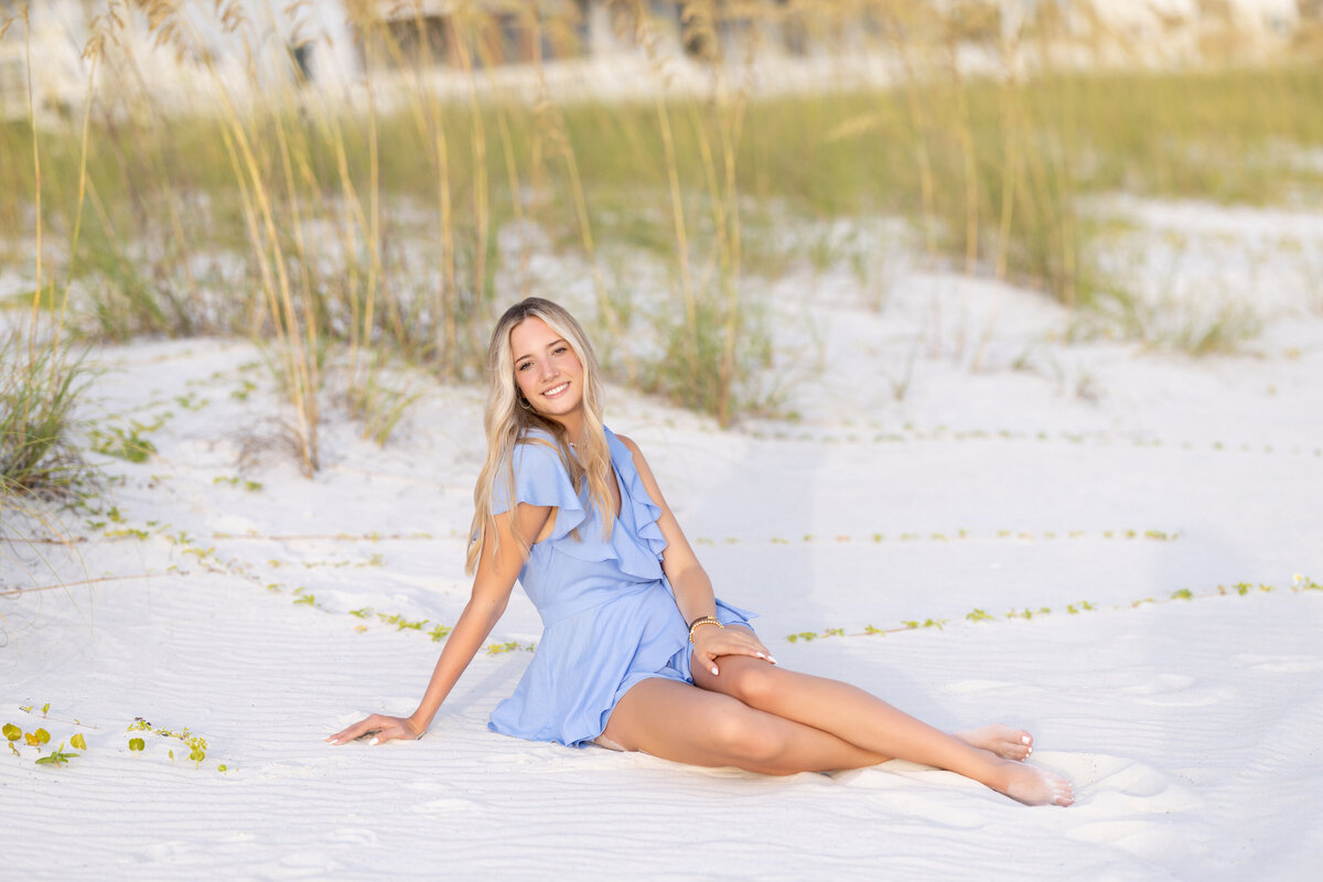 A girl sitting on a beach leaning back on one arm