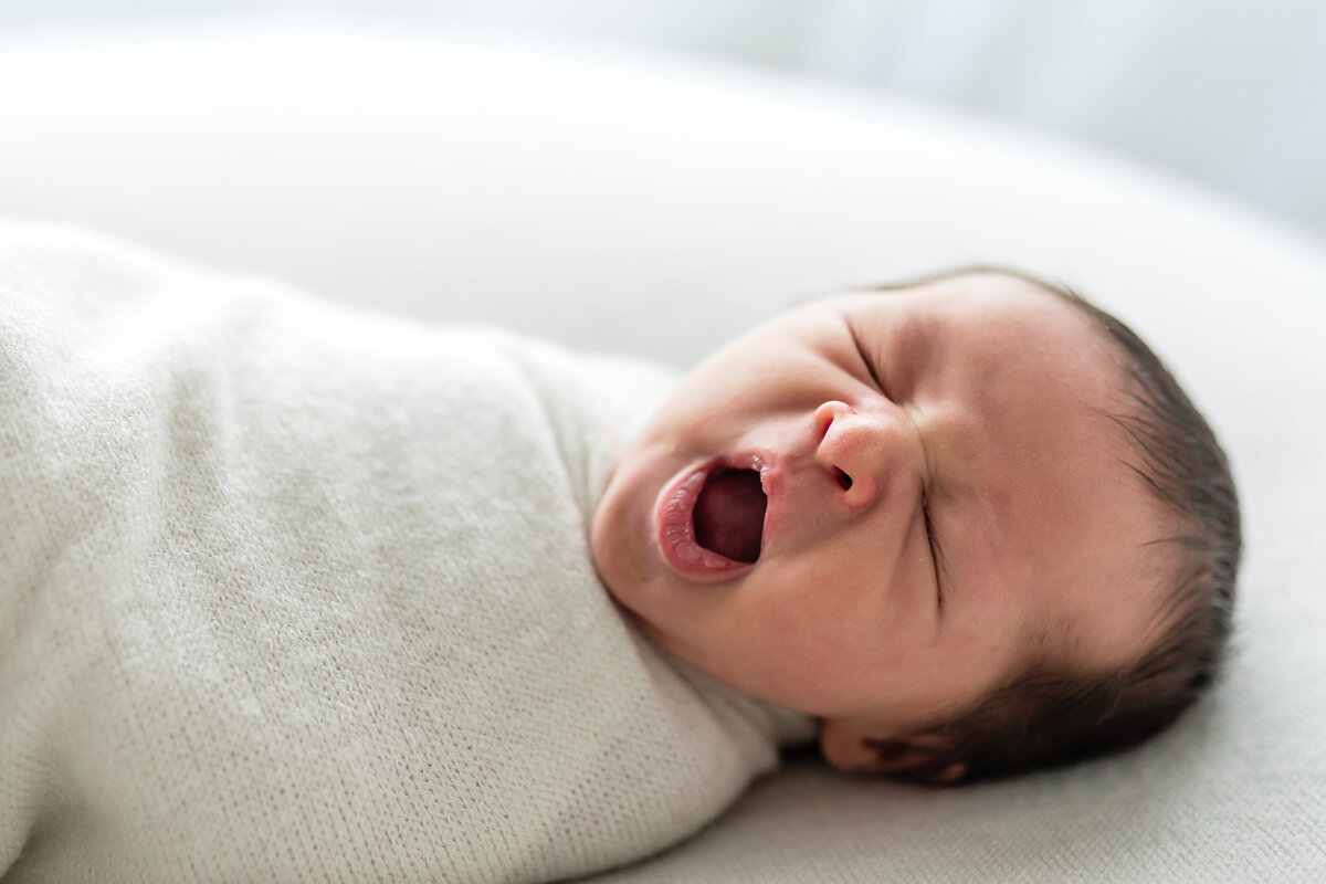 baby yawning while laying on soft white blanket