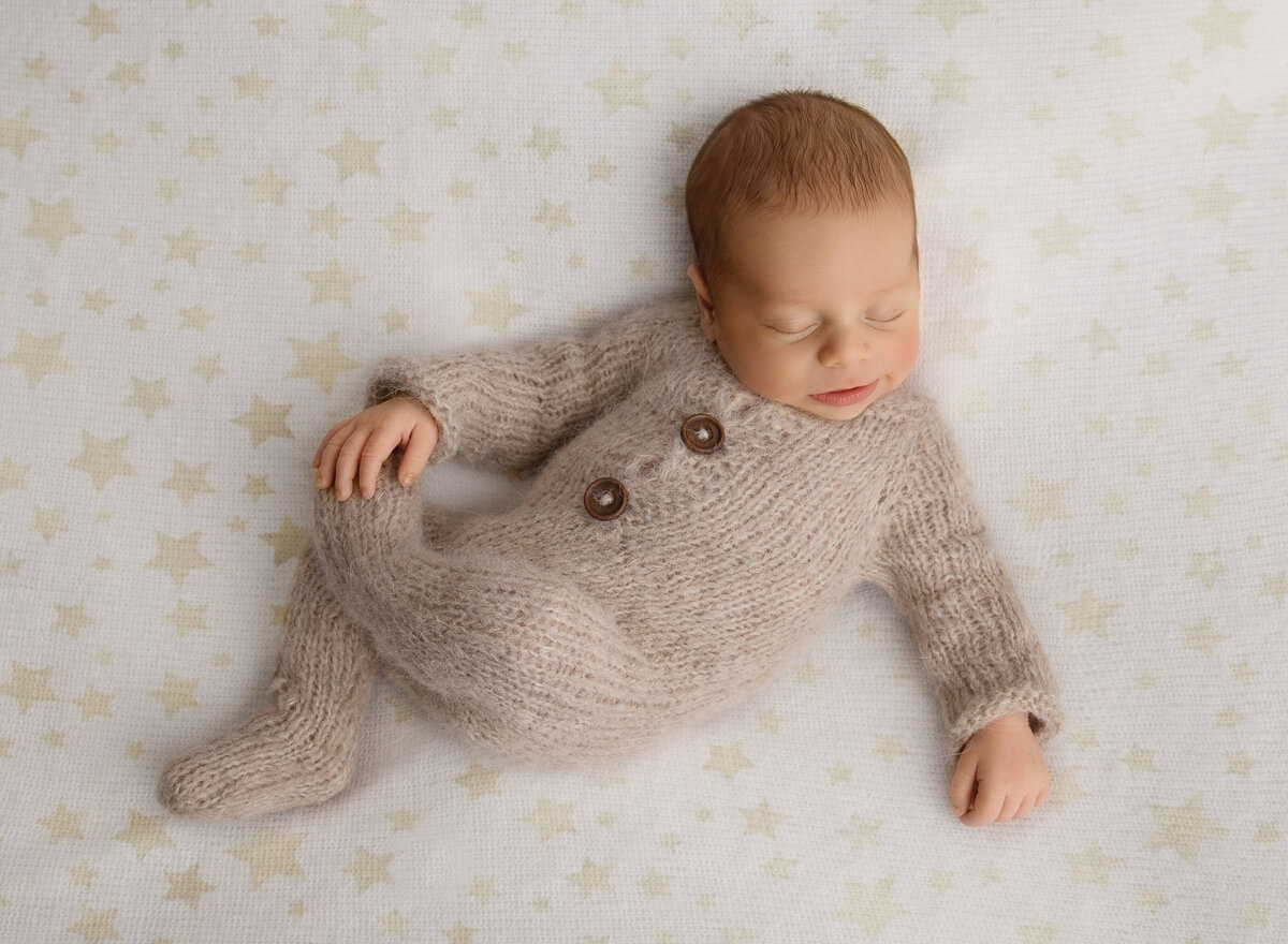 Baby boy in beige knit jumper holding his does for a newborn photoshoot. Captured by top Brooklyn, NY newborn photographer Chaya Bornstein Photography.