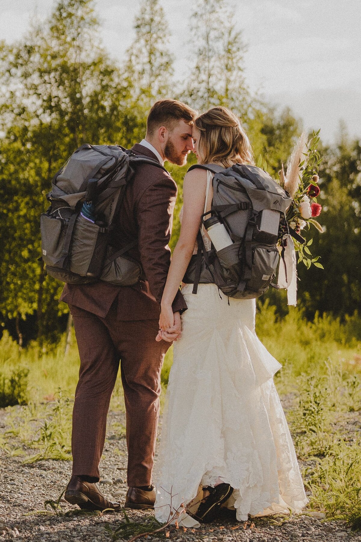 A couple wears their matching hiking backpacks while dressed in their wedding day attire