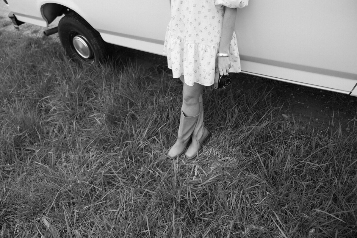 woman sitting quietly in the Kansas tall grass wearing a floral dress on a calm cloudy day holding a vintage camera