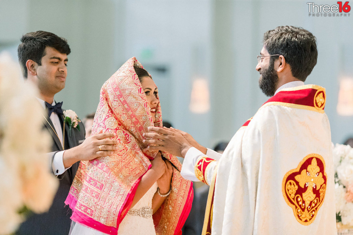 Bride goes through an Indian wedding ritual from the officiant as the Groom looks on