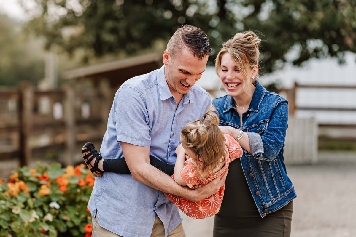 Maternity session filled with joy as mom and dad laugh while watching their daughter play, capturing a lively family moment.