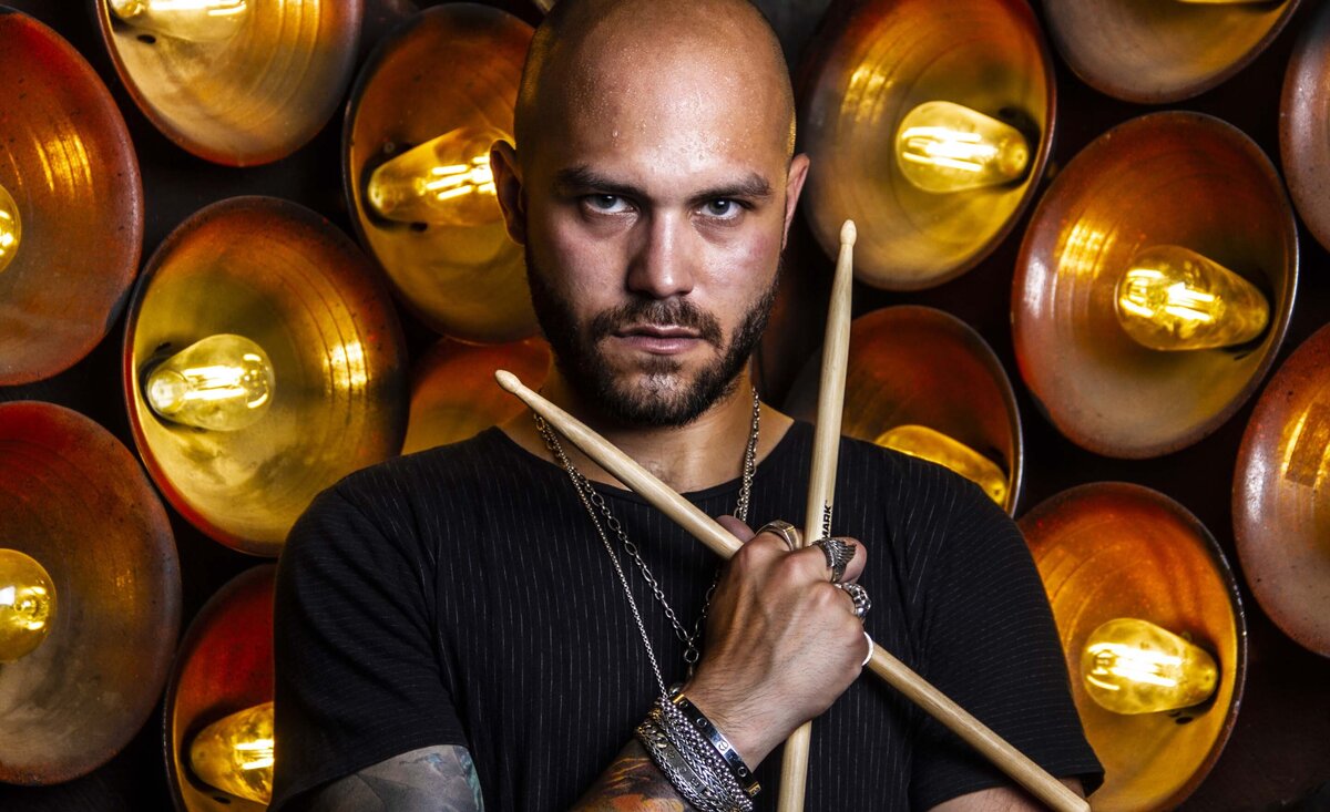Male musician portrait Left Of The Slash holding drum crossed sticks with circle gold lights background
