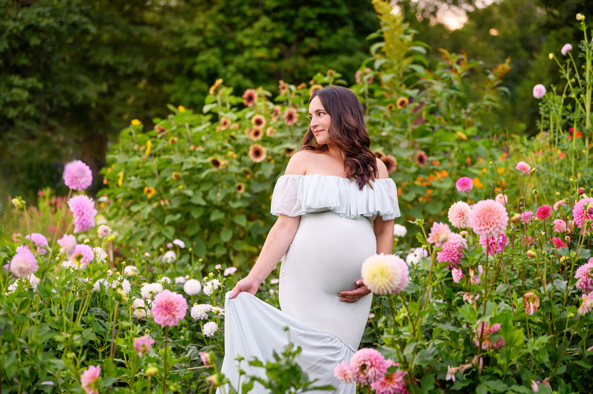 Woman wearing a mint green maternity dress standing in a field of flowers for her Toronto Maternity Photographer Session.