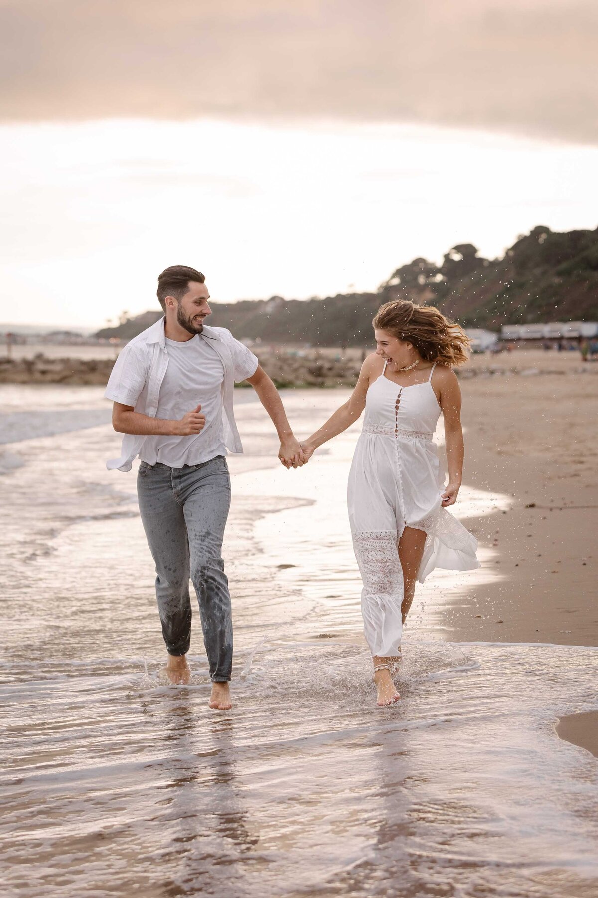 A couple running on the seashore hand in hand with splashes of water