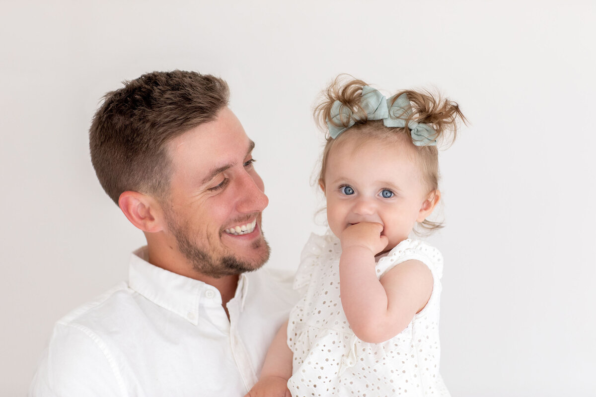 Father holding his young daughter in his arms as she smiles brightly, capturing a sweet and loving moment between the two during their Bucks County family photo session