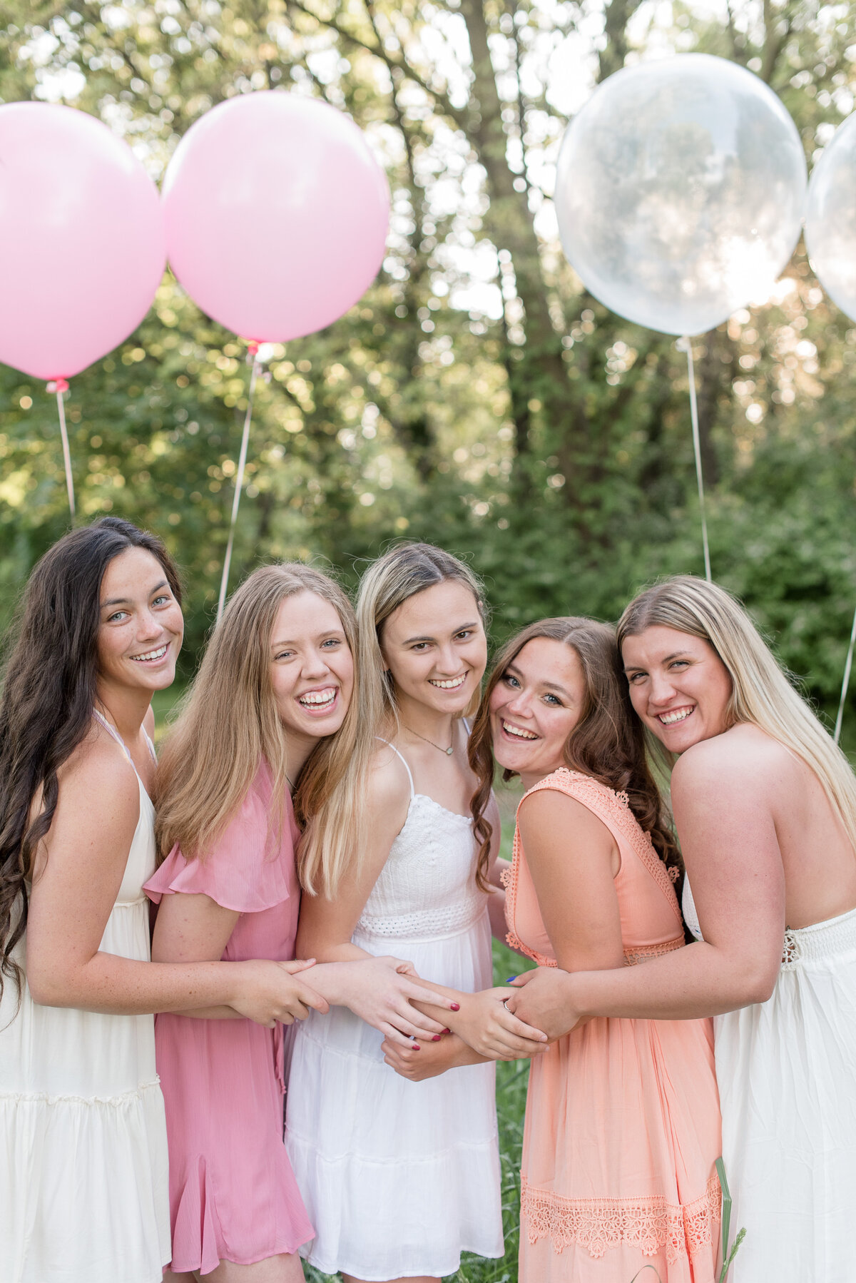 Five Senior girls huddled together at Lancaster County Park wearing shades of pink, orange, and white.