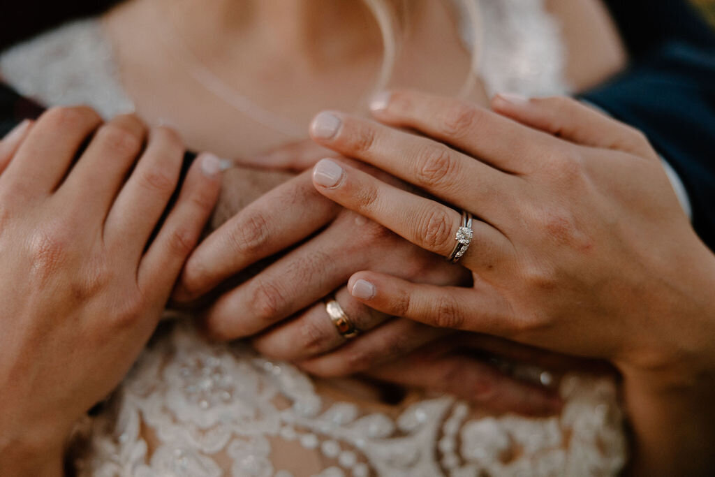 Gorgeous vintage looking wedding photography by Morgan Ashley Lynn Photography in Lake Country, Wisconsin of a closeup of bride and groom's hands on top of eachother, wrapped around the bride's chest displaying their wedding rings