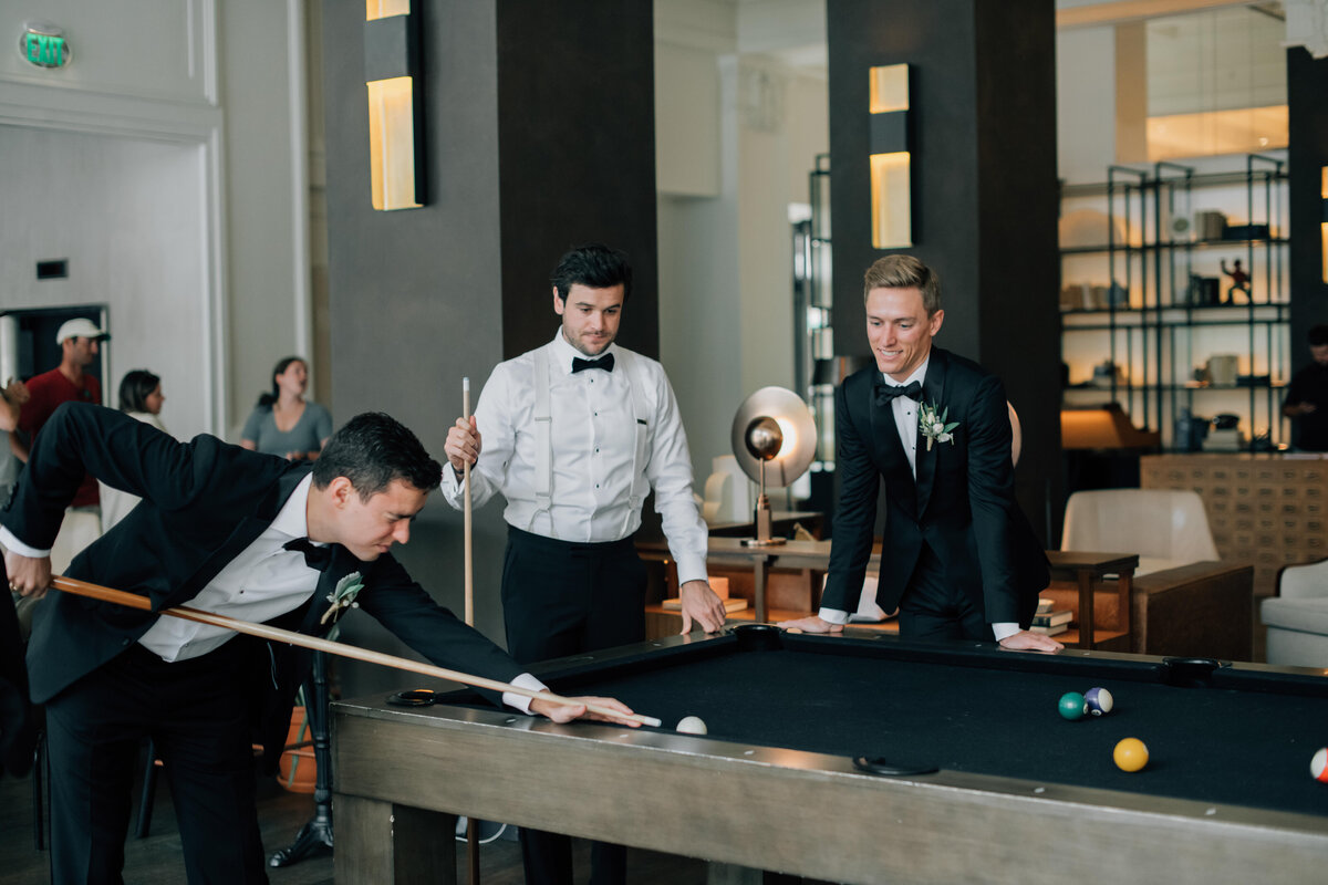 Photo of the groom and groomsmen playing pool in the lobby of the Surety Hotel. Photo by Anna Brace, a wedding photographer in IA. 