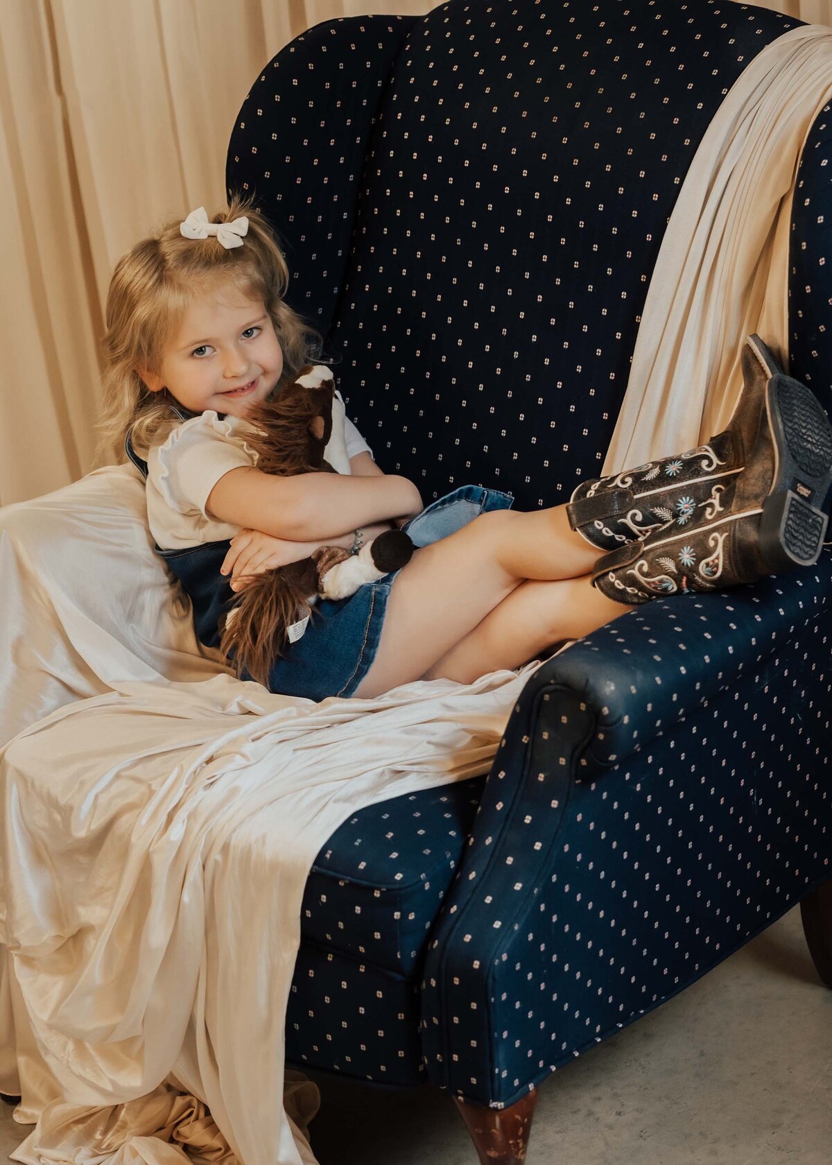 Maddie Rae Photography little girl laying across a chair with her legs crossed and she is hugging a stuffed animal