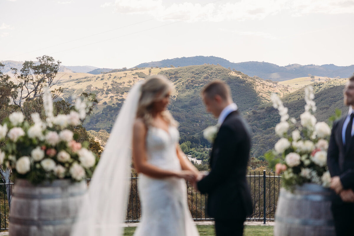 Blurred image of a bride and groom during their wedding ceremony with focus on the view in the background - mountains and the valley down to the Murrumbidgee River at Brindabella Hills Winery