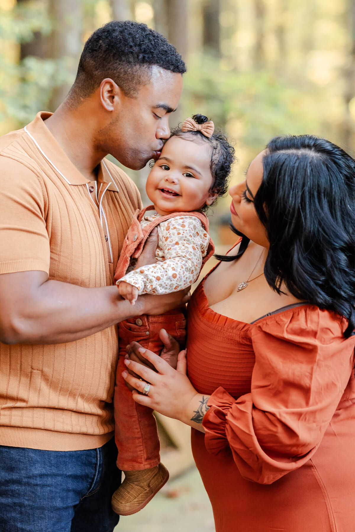 A dad kisses his toddler daughter on the forehead while the mom looks on lovingly during a family photo session.
