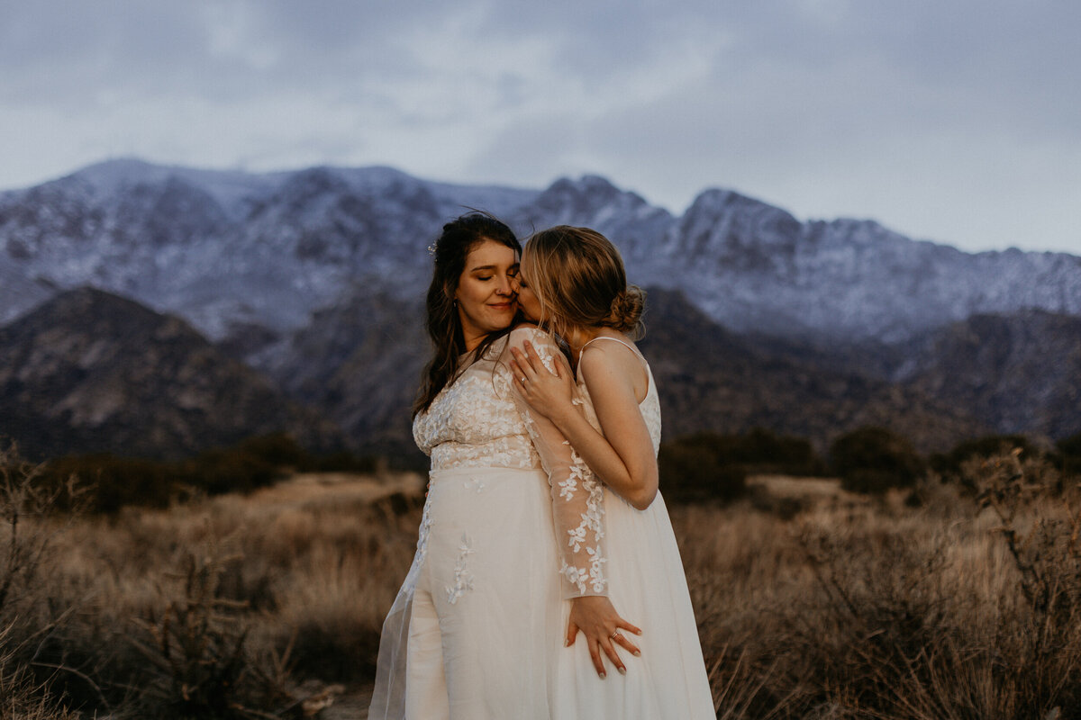 newlywed brides holding each other in front of the Sandia mountains in Albuquerque, New Mexico