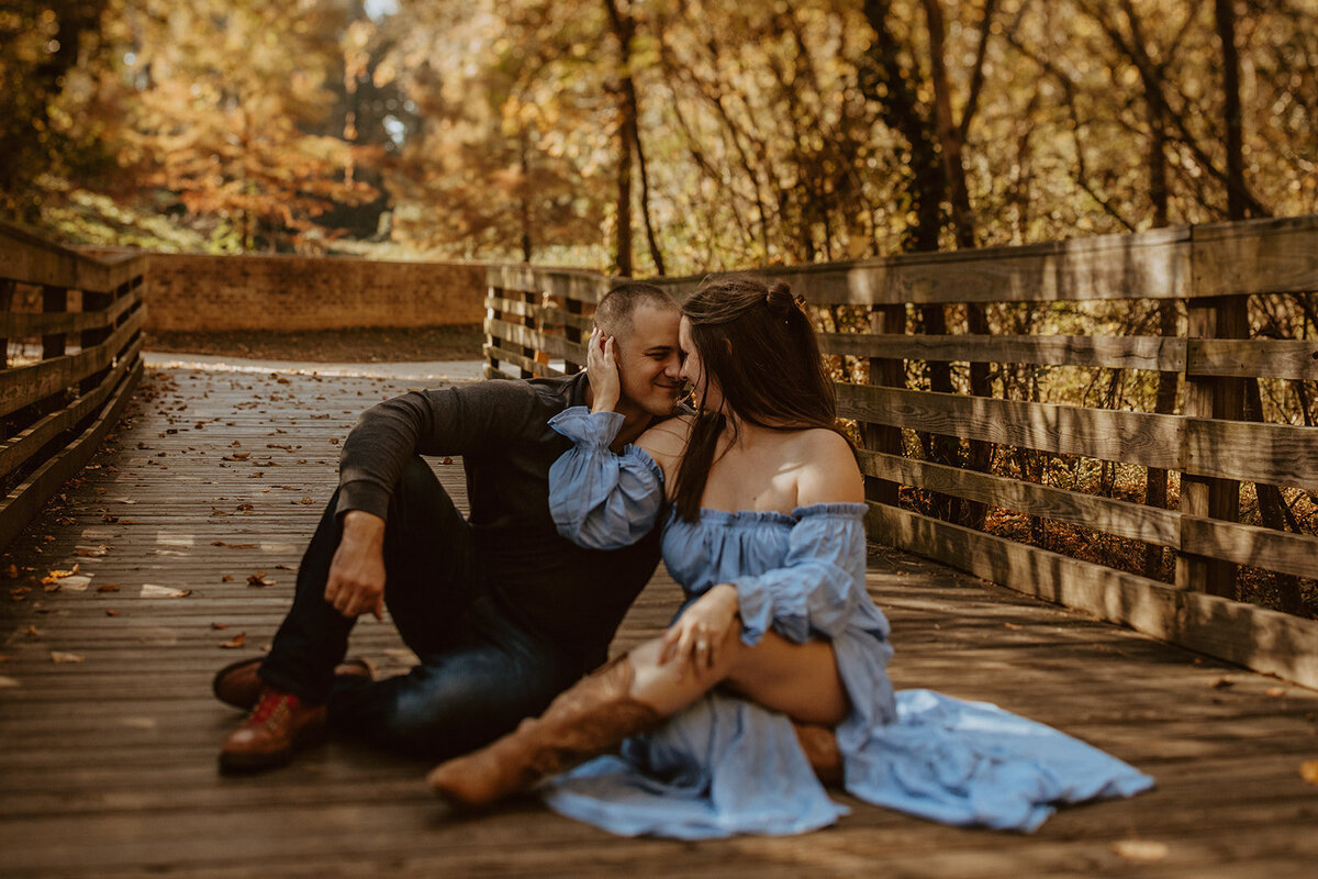 girl in blue dress kisses man while sitting on bridge