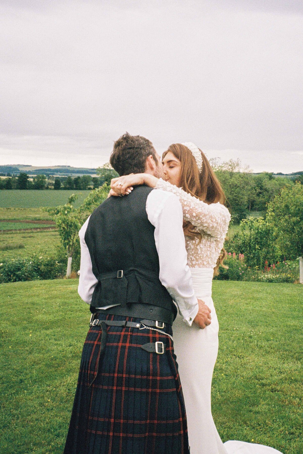 A bride and groom are photographed as they wrap their arms around each other and kiss.