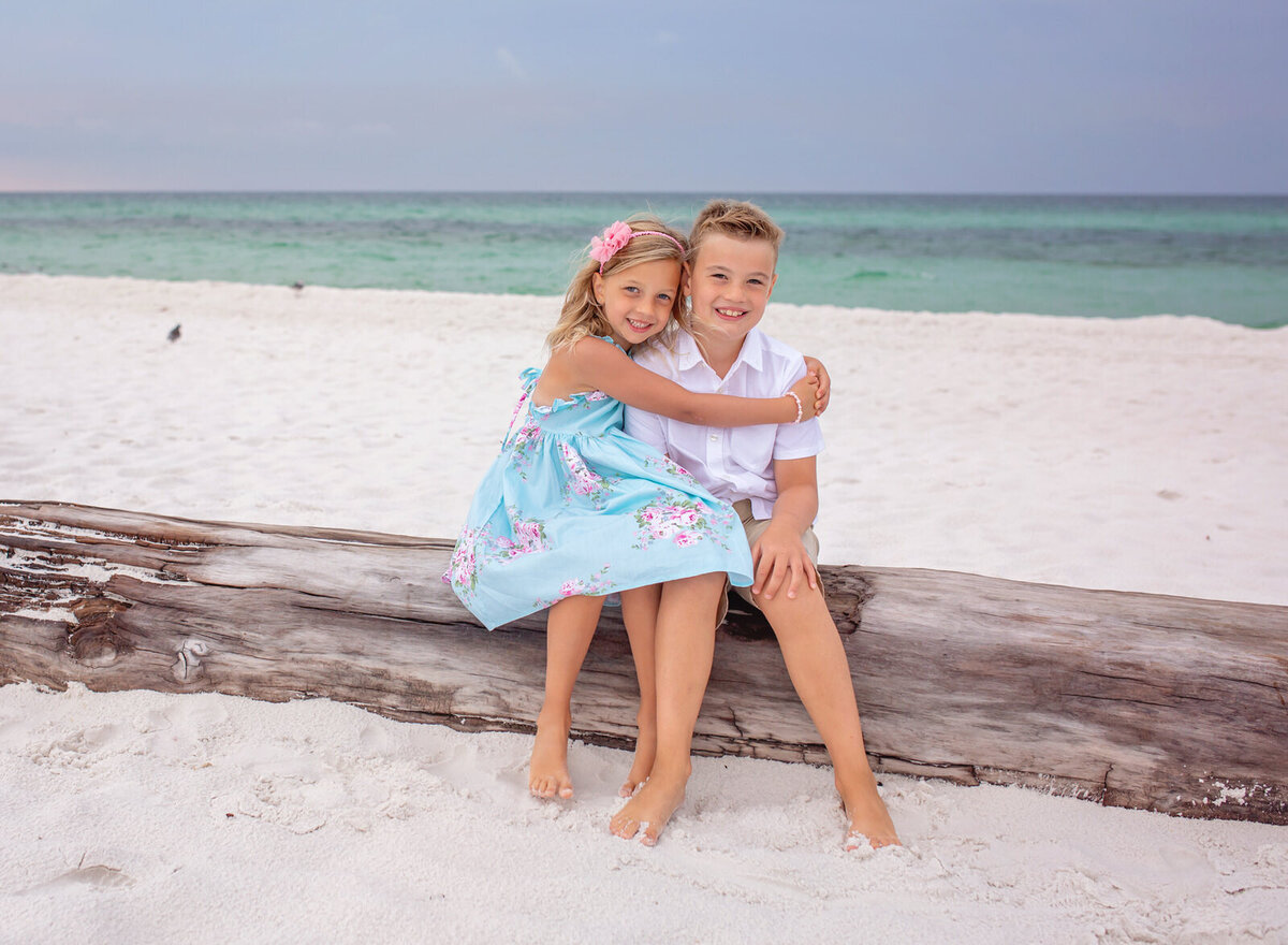 young-brother-and-sister-posing-on-driftwood-in-navarre-beach