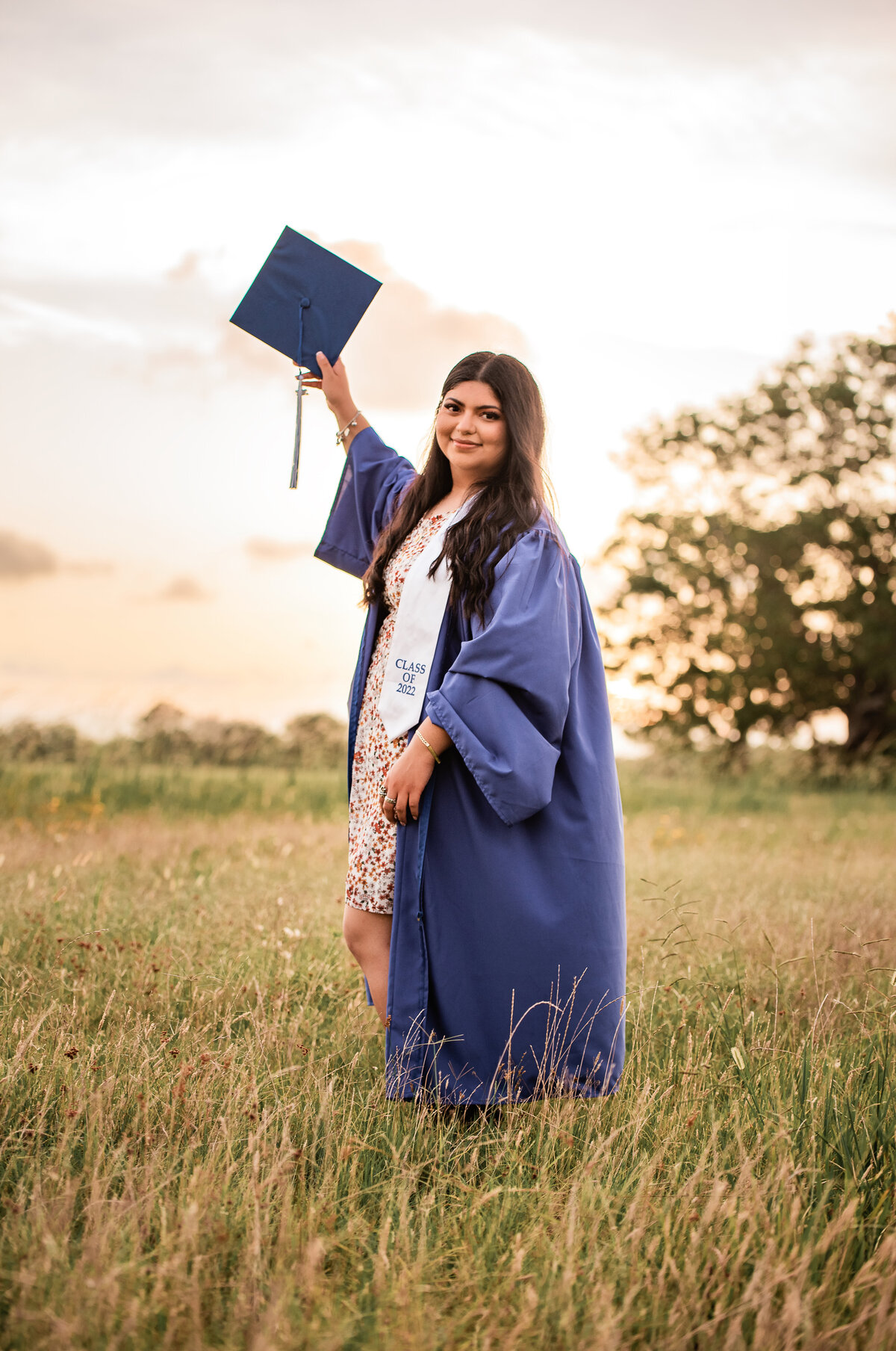 A Houston area senior stands in a field holding her cap in the air in celebration of her upcoming graduation.