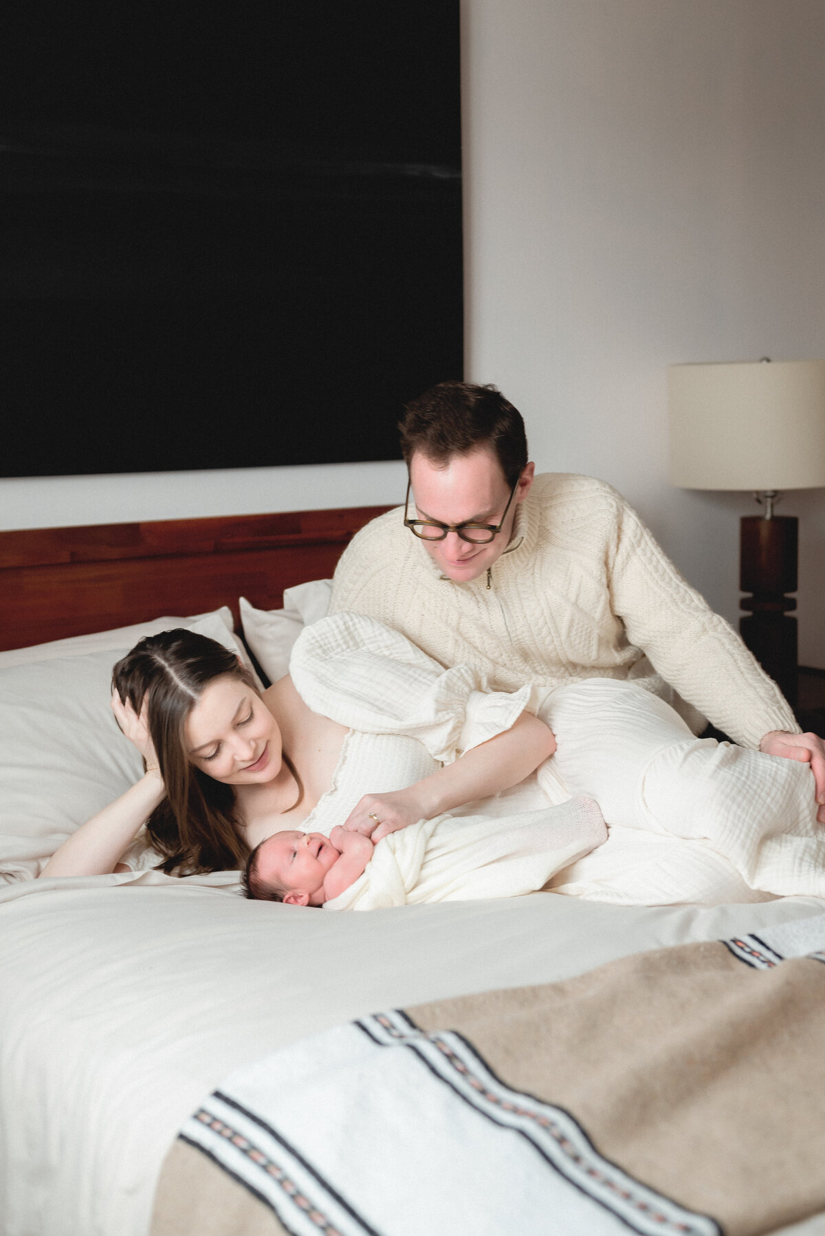 Parents sitting on bed looking down at newborn