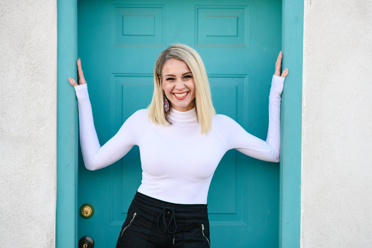 A branding photographer in littleton takes a picture of a business owner standing in front of a turquoise door in downtown Littleton for her Littleton branding photos during a littleton branding photography session.