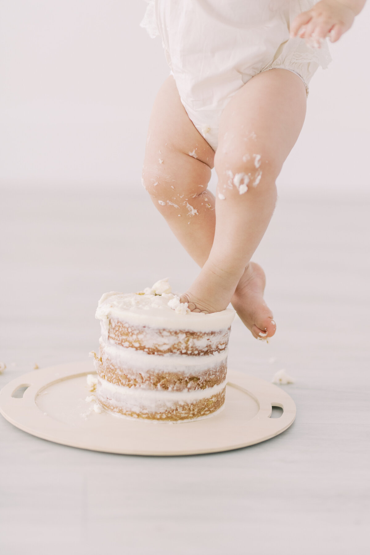 Baby girl standing on top of birthday cake at Pearle Studios, tiny toes covered in frosting